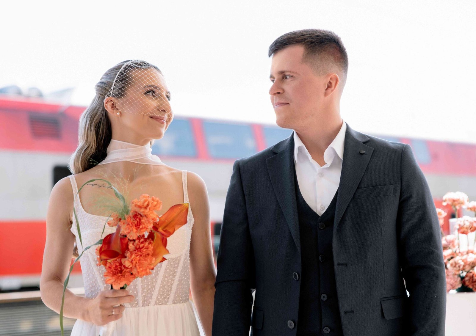 Bride with orange flowers and groom at a train station on their wedding day