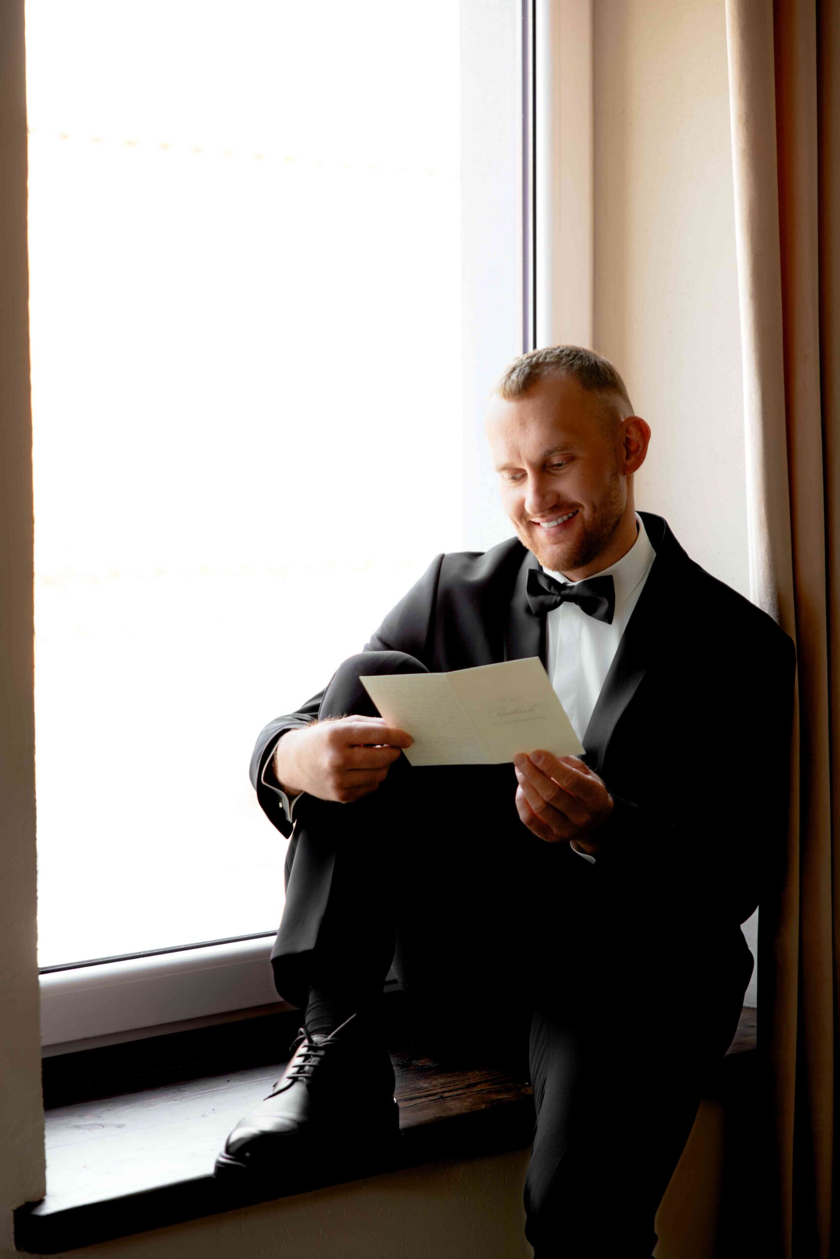 groom reading letter from bride on morning sitting on window