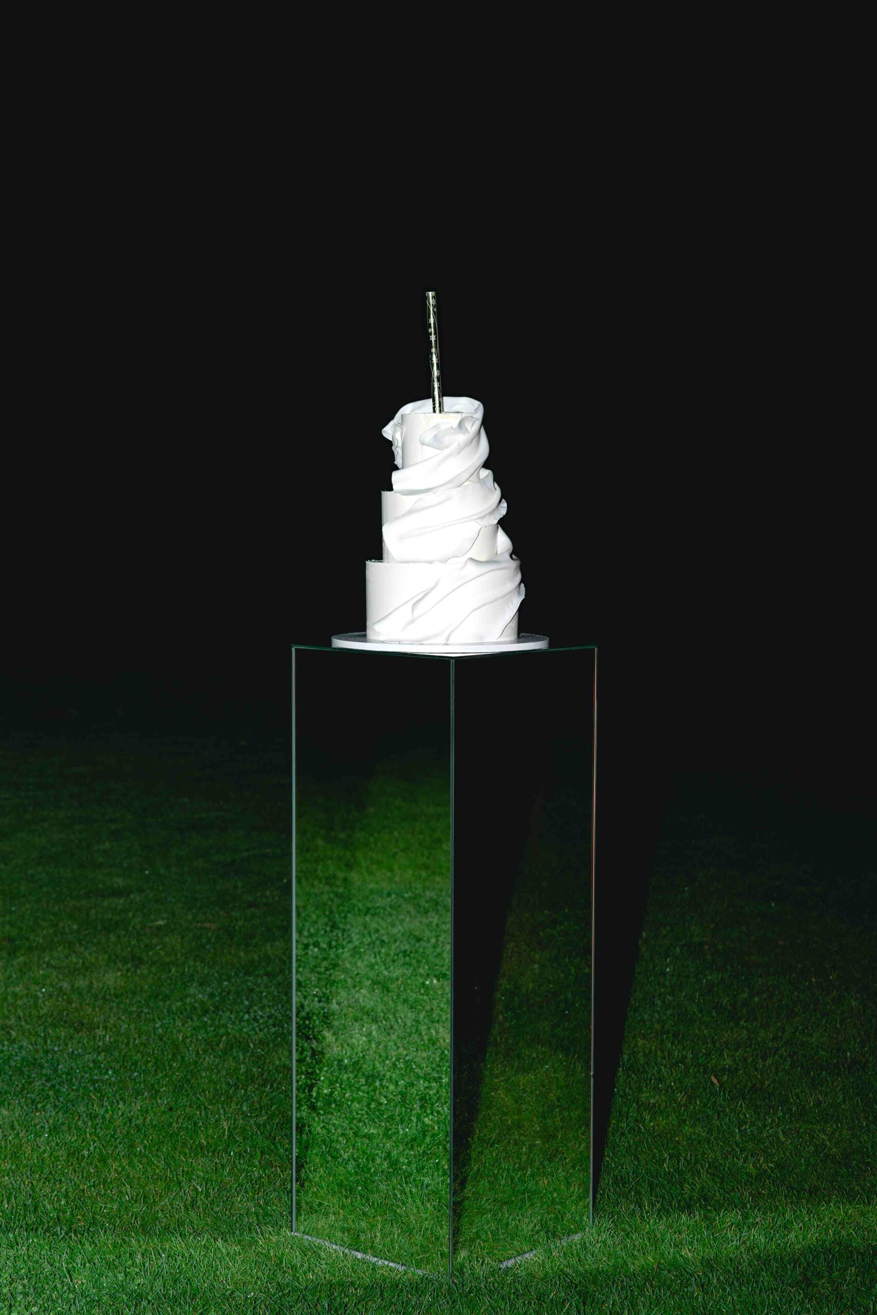 white wedding cake in night on grass on glass stand