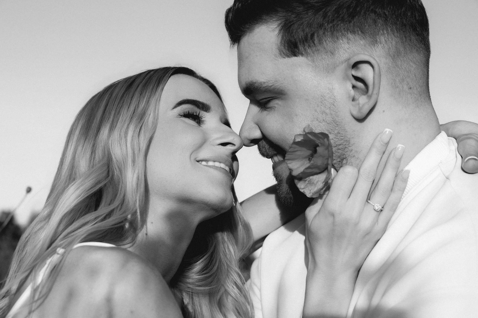 Black and white close up of a couple with a poppy near their faces