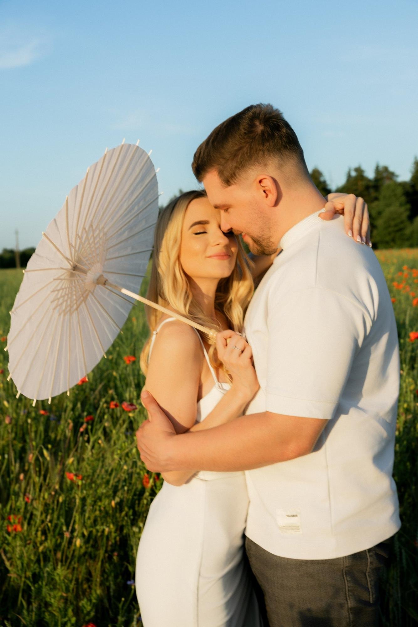 Couple embracing under a white paper parasol in the field