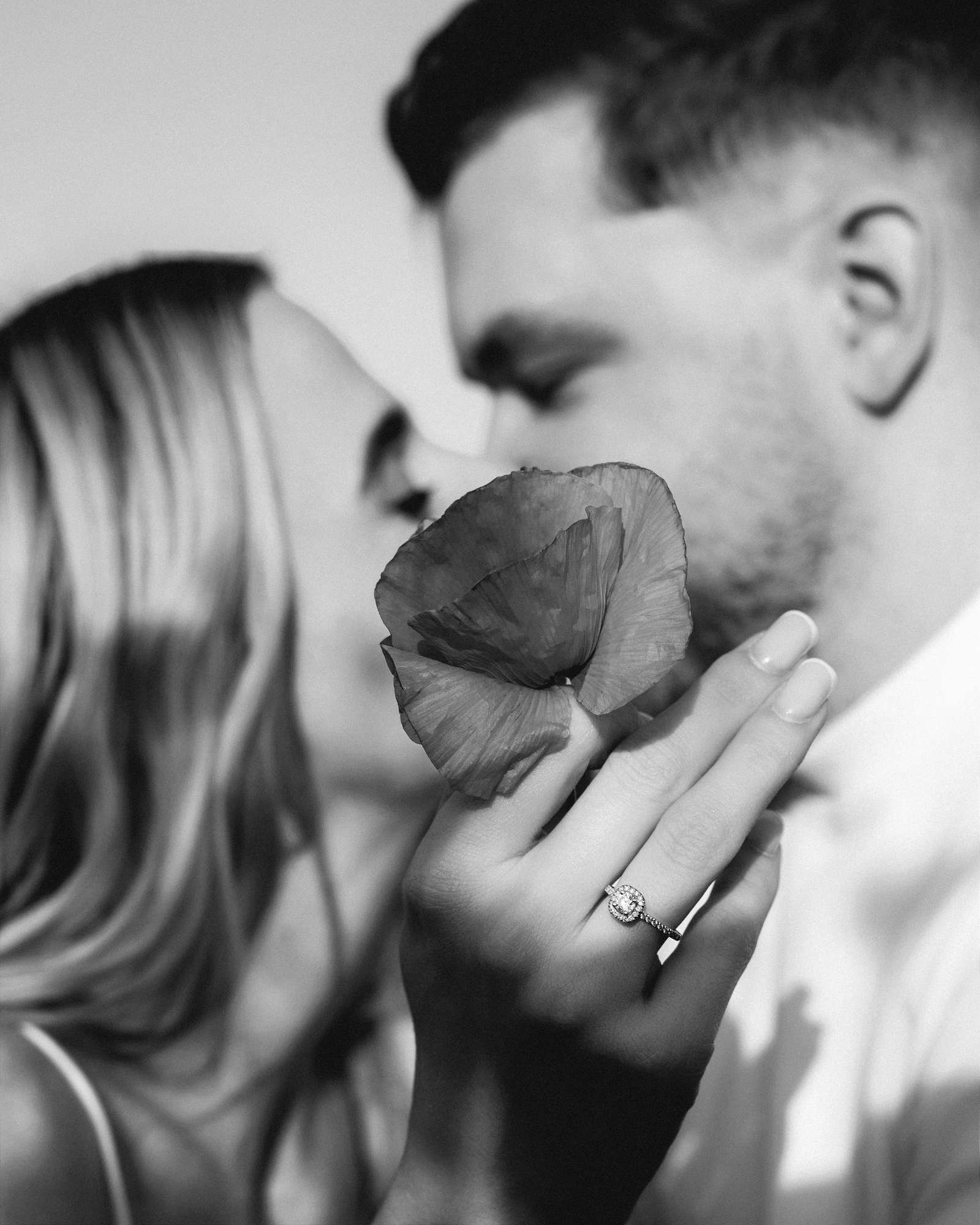 Couple about to kiss, holding a poppy petal between them, black and white