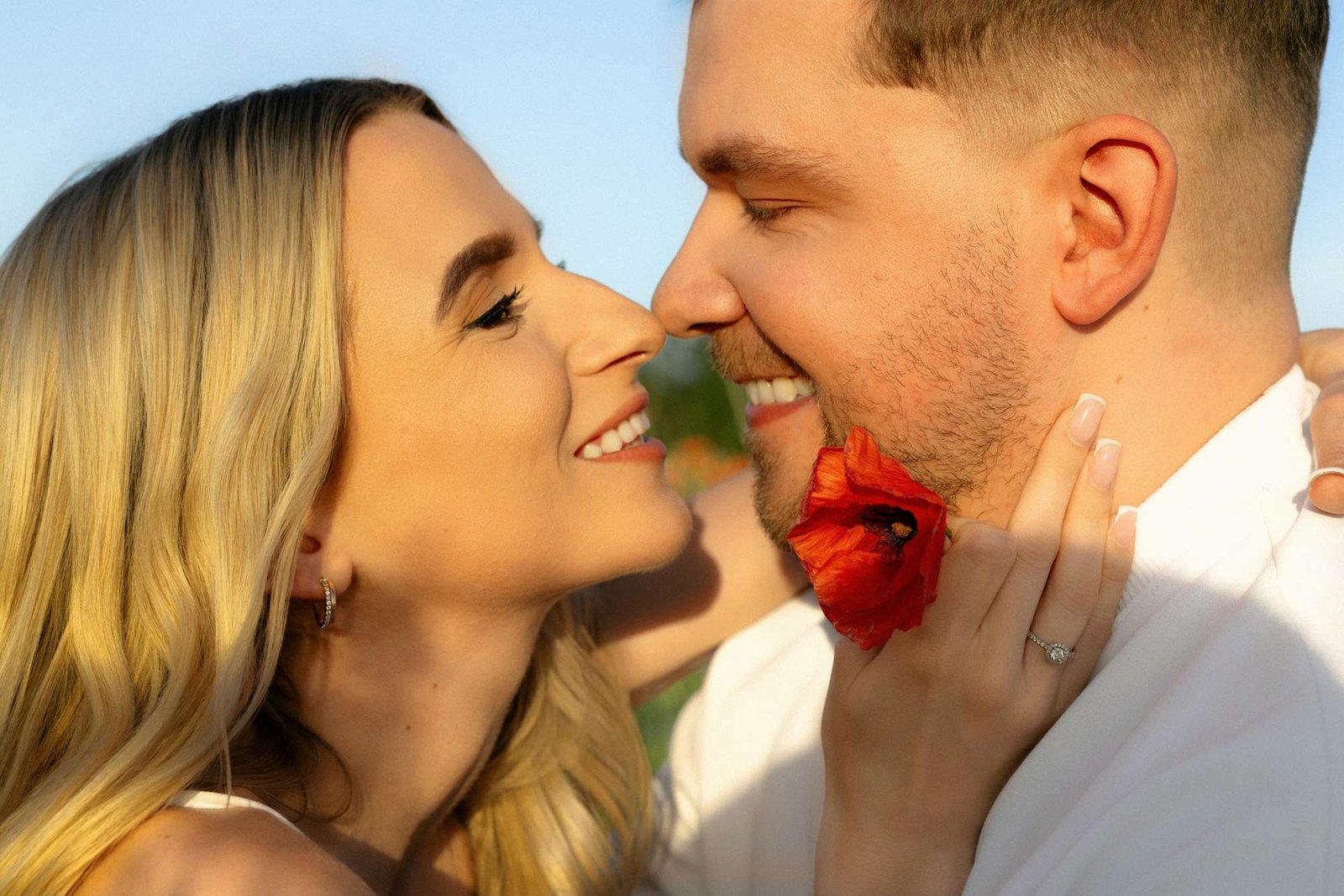 Couple laughing close together with a poppy flower between their faces