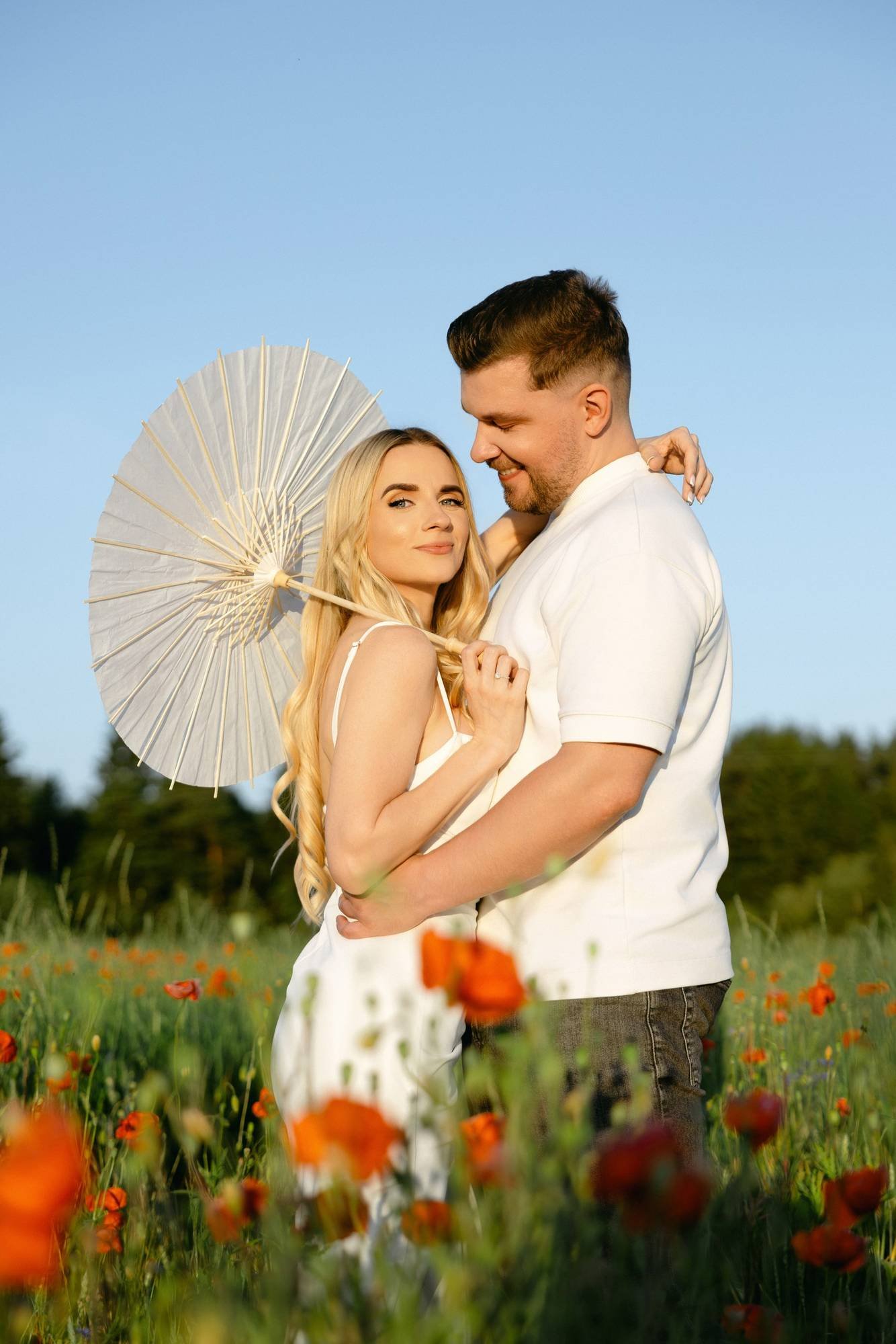 Couple smiling and embracing under a white parasol in the field