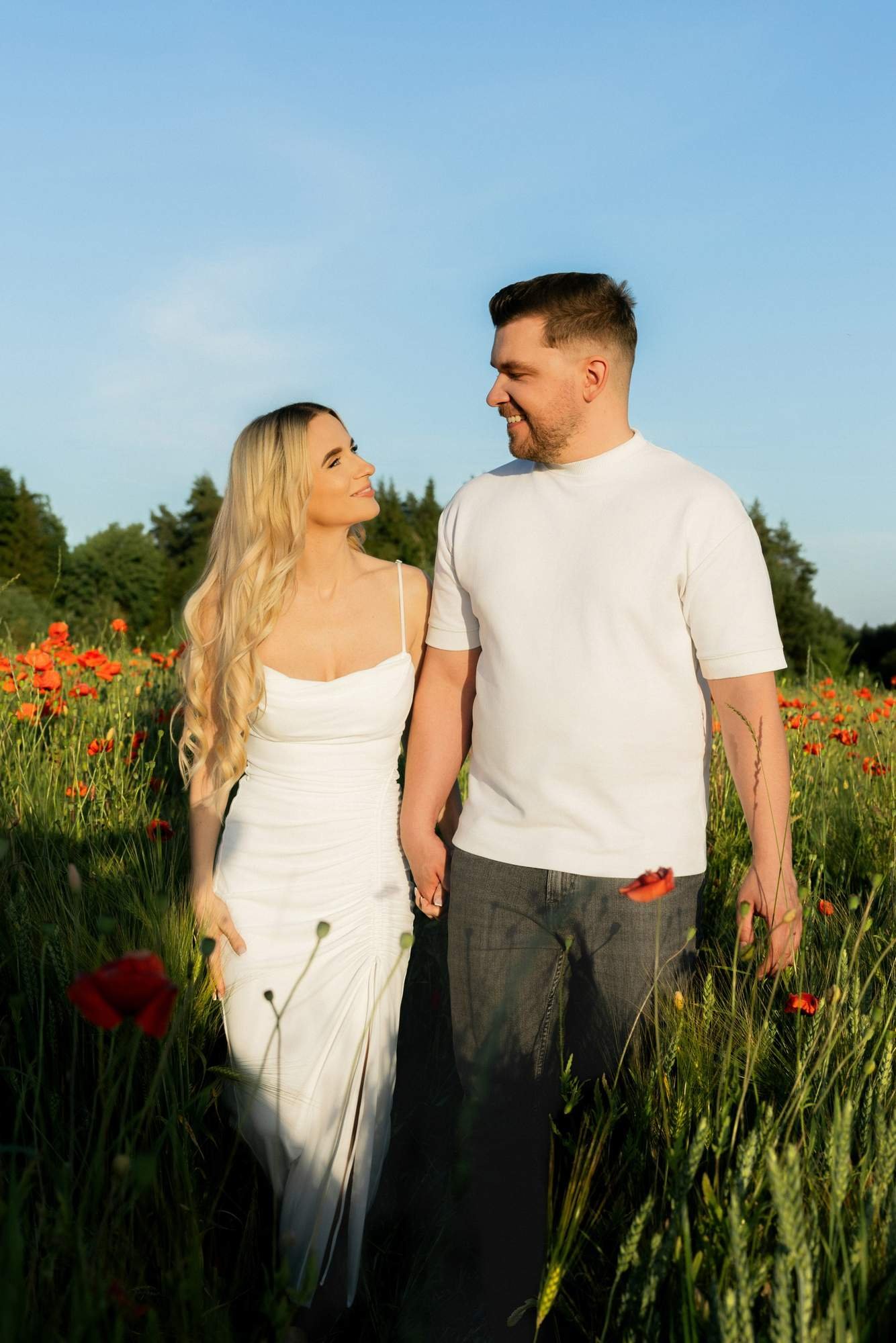 Couple standing side by side in a meadow under a clear blue sky