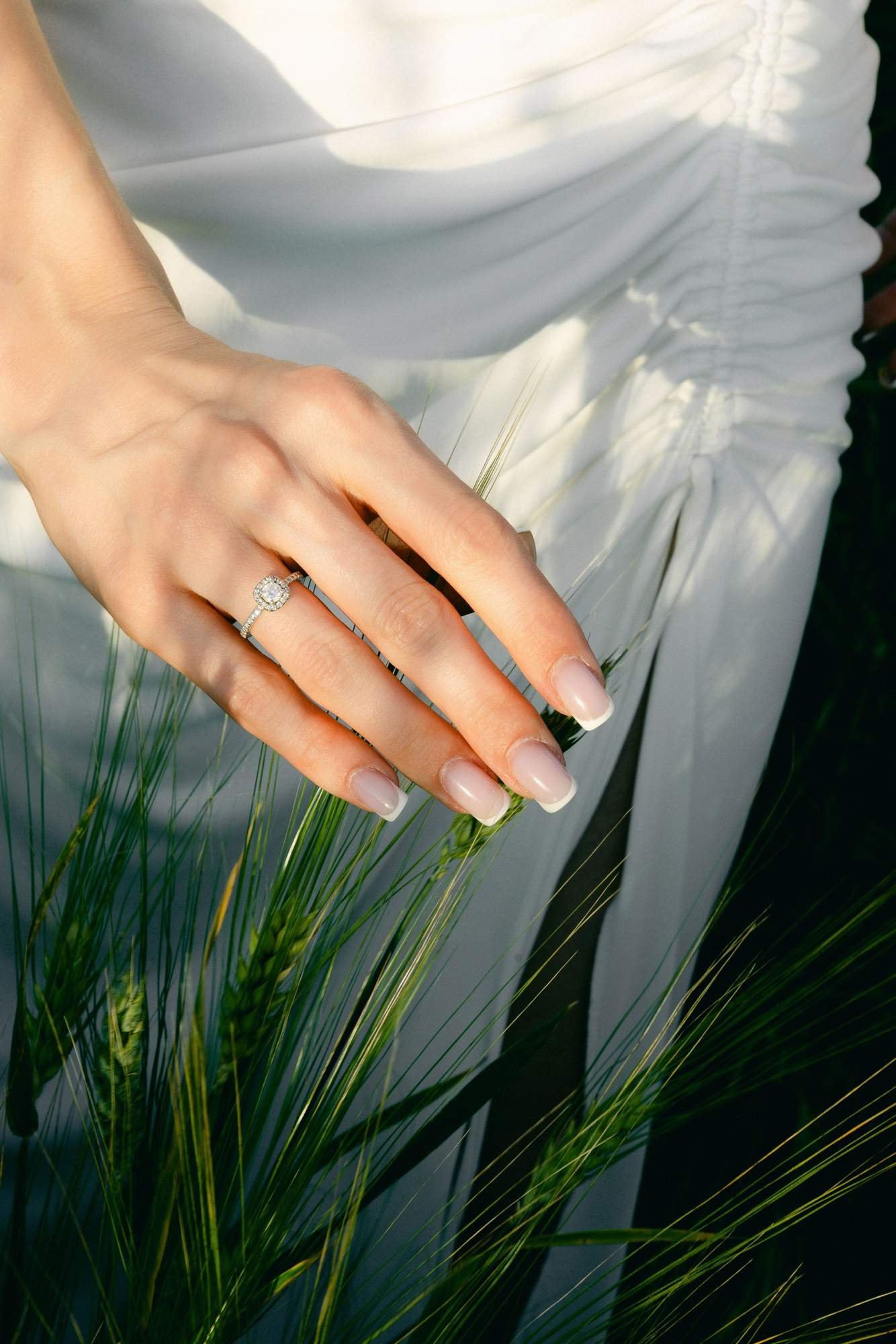 Close up of an engagement ring resting against wheat in the field
