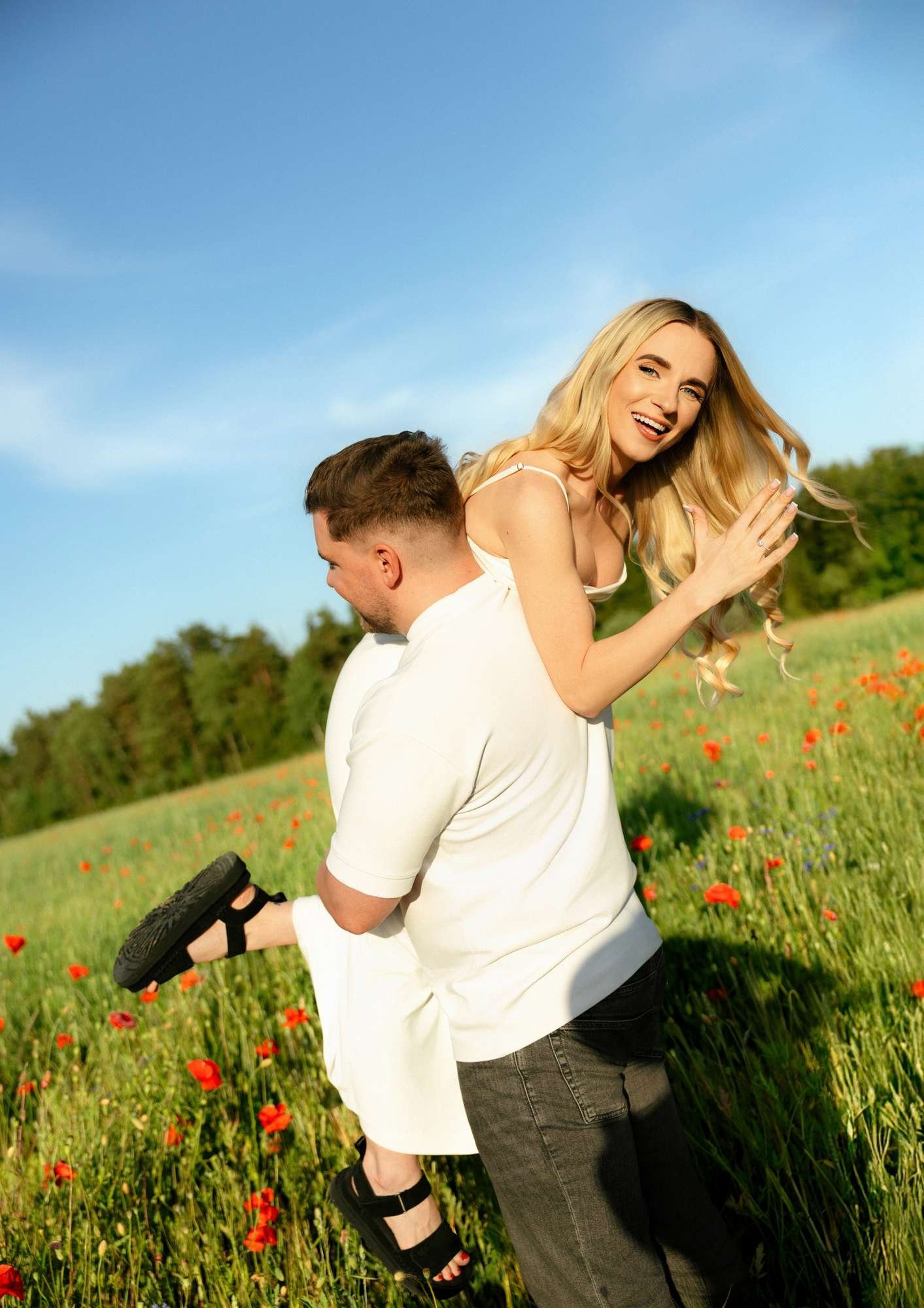 Groom-to-be carrying his fiancee piggyback style through a poppy field, both laughing