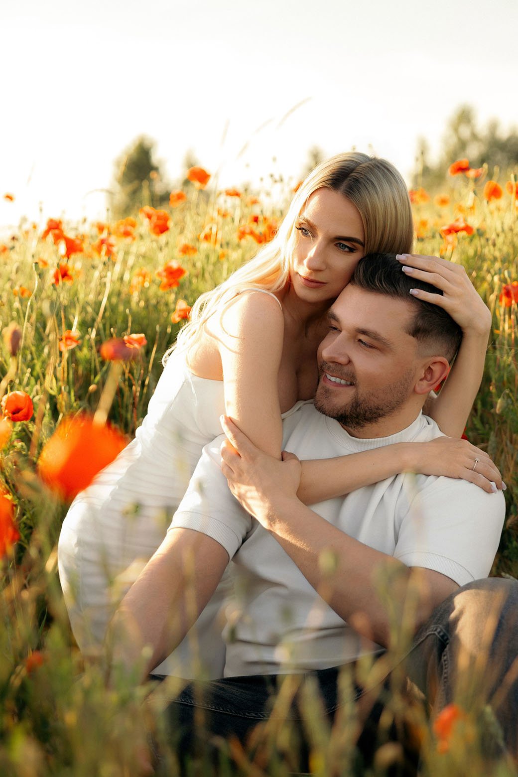 Couple hugging in a poppy field with golden hour sun behind them