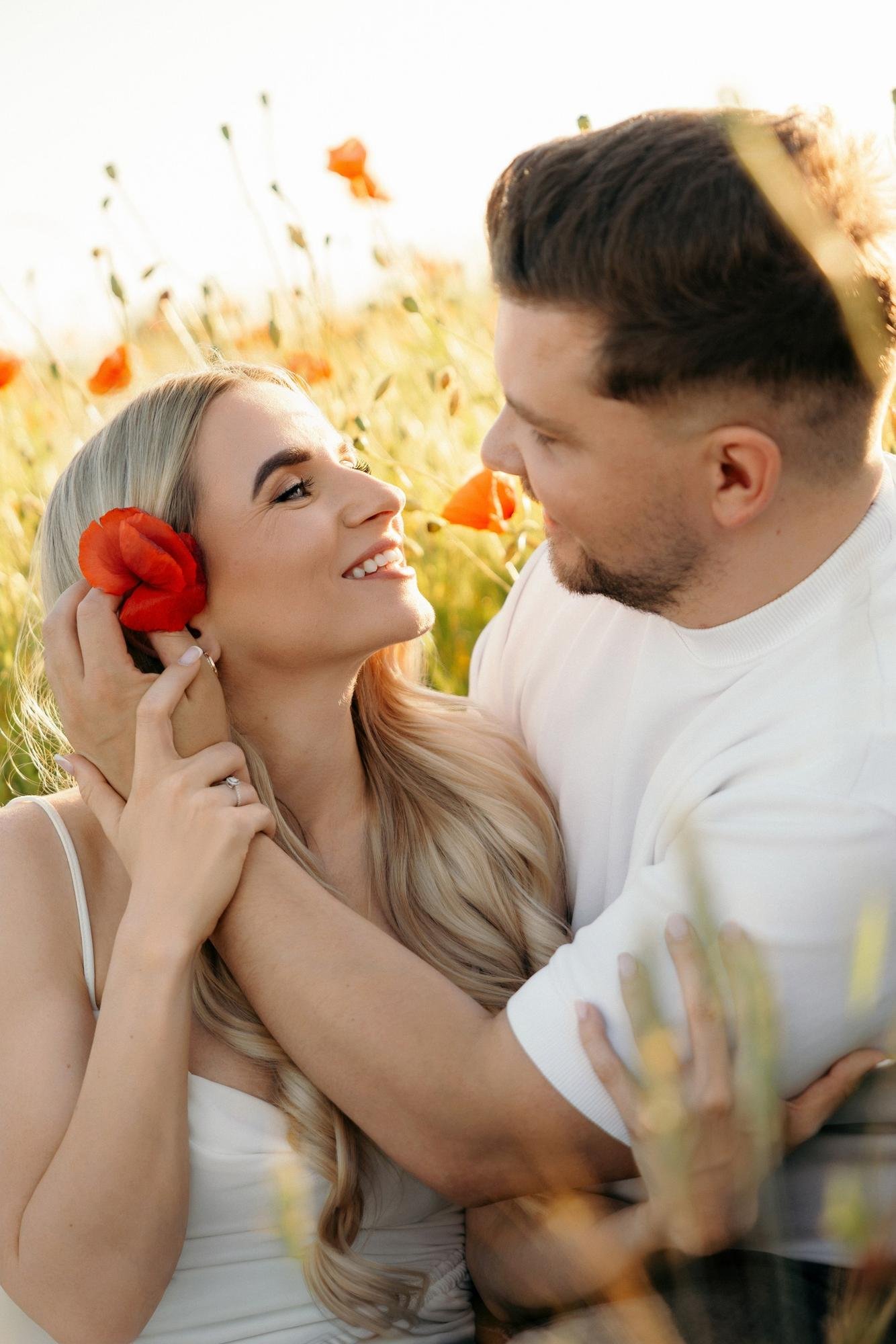 Woman holding a red poppy near her ear while her partner looks at her, smiling