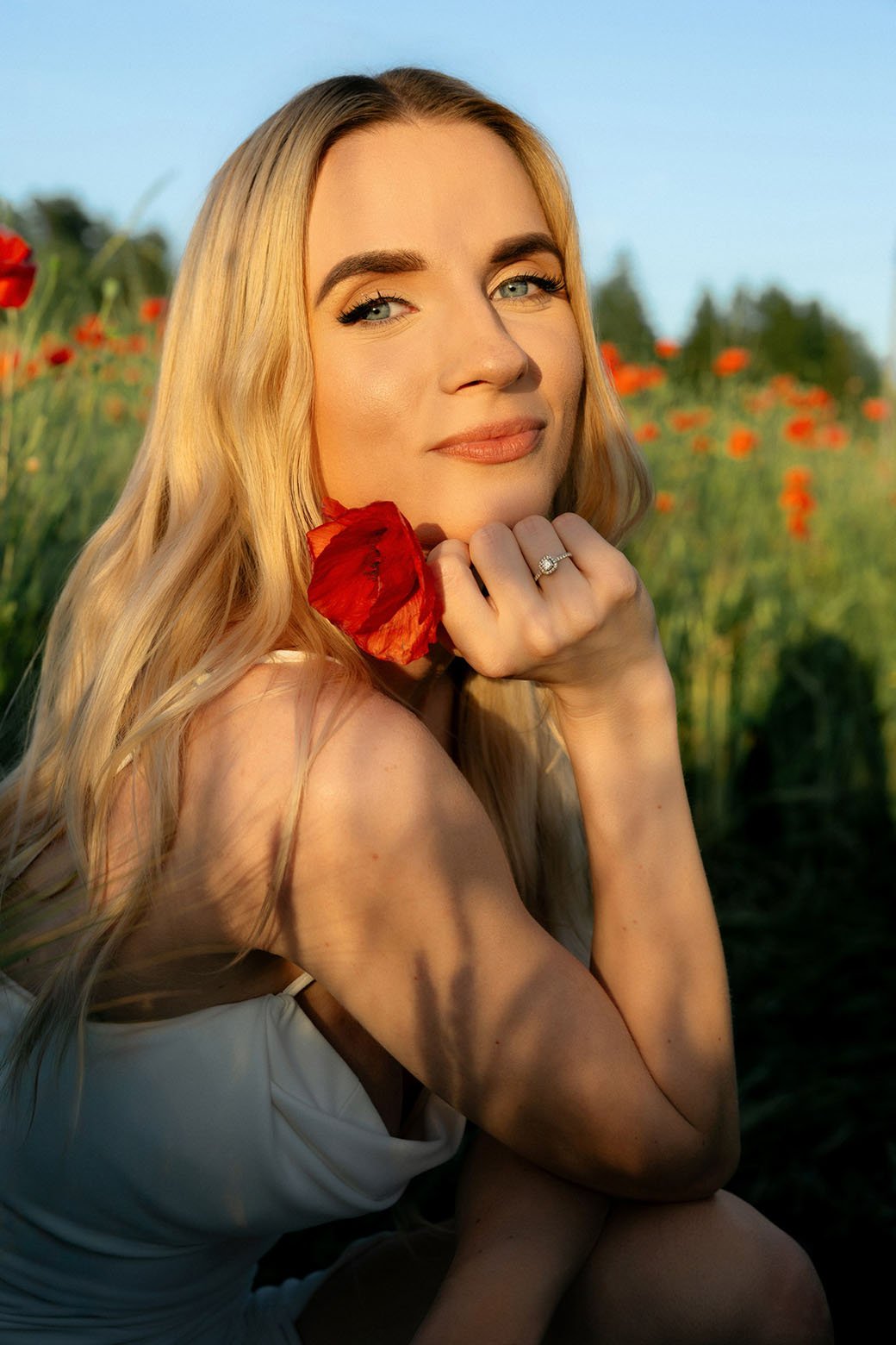 Woman holding a red poppy next to her face, smiling