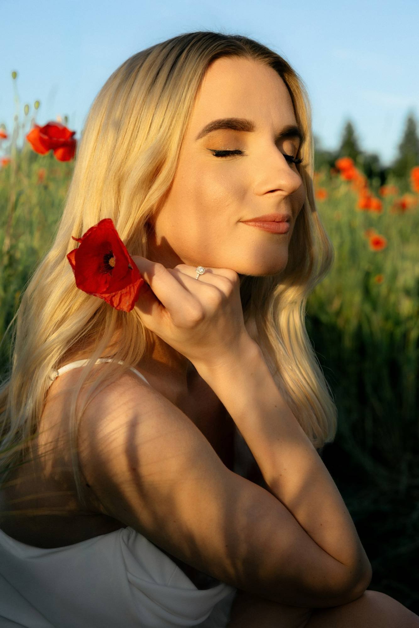 Woman with her eyes closed holding a poppy near her cheek in golden light