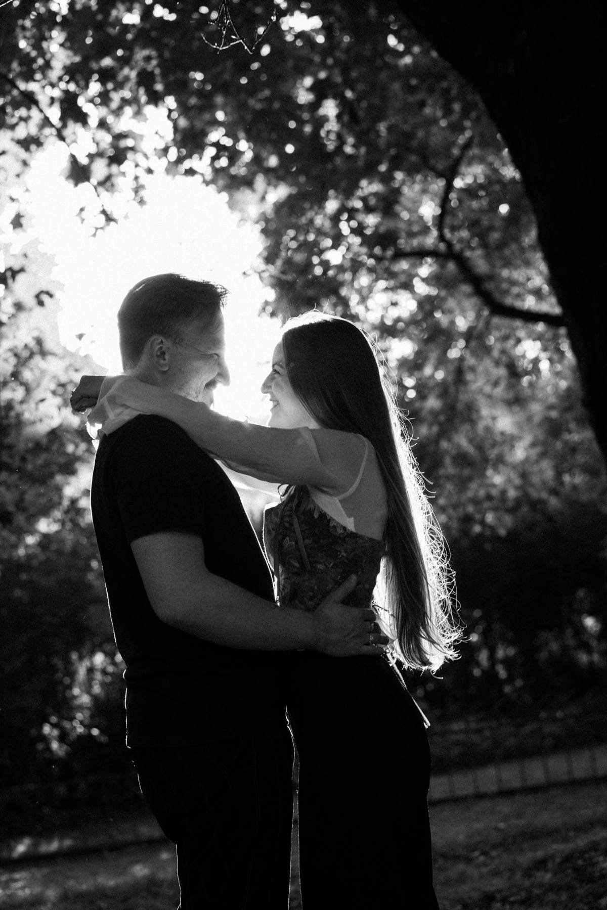Backlit black and white portrait of the couple embracing in the park.