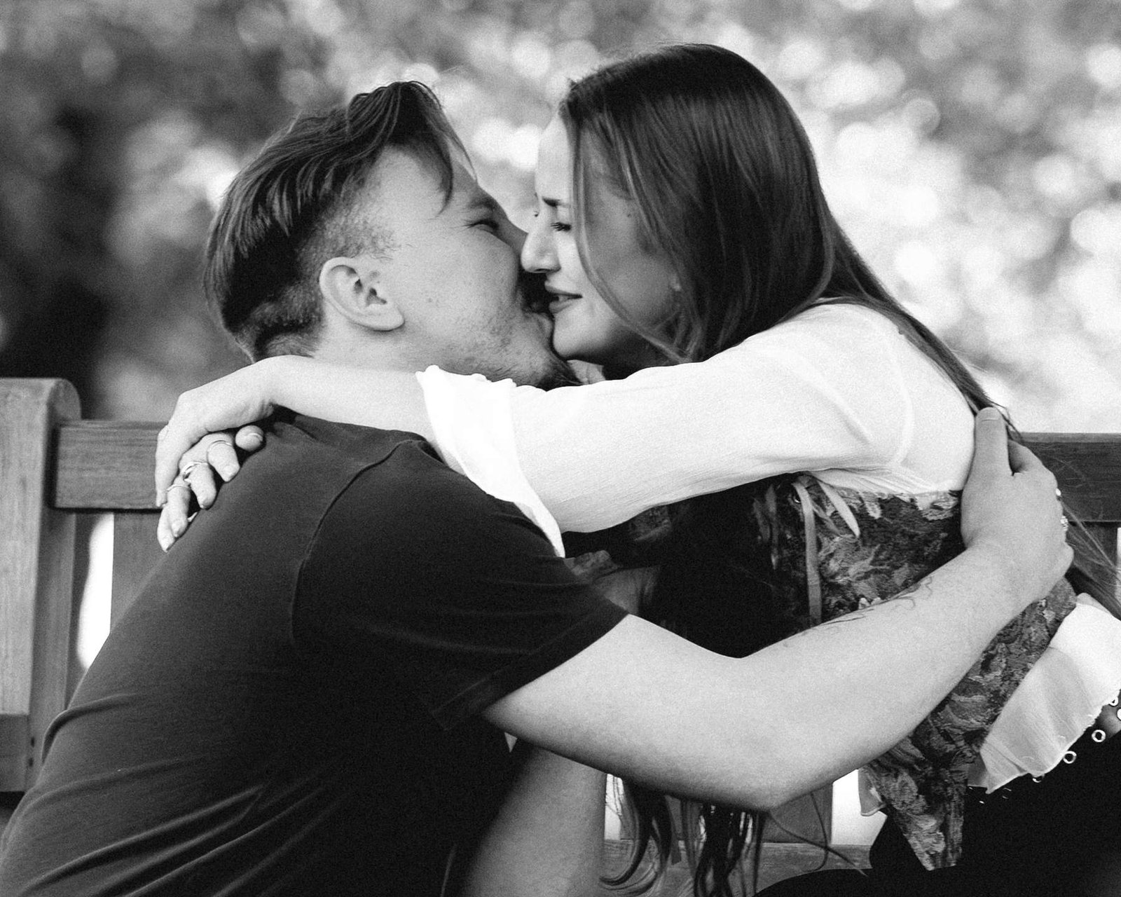 Newly engaged couple kissing on a park bench moments after the surprise proposal, black and white.