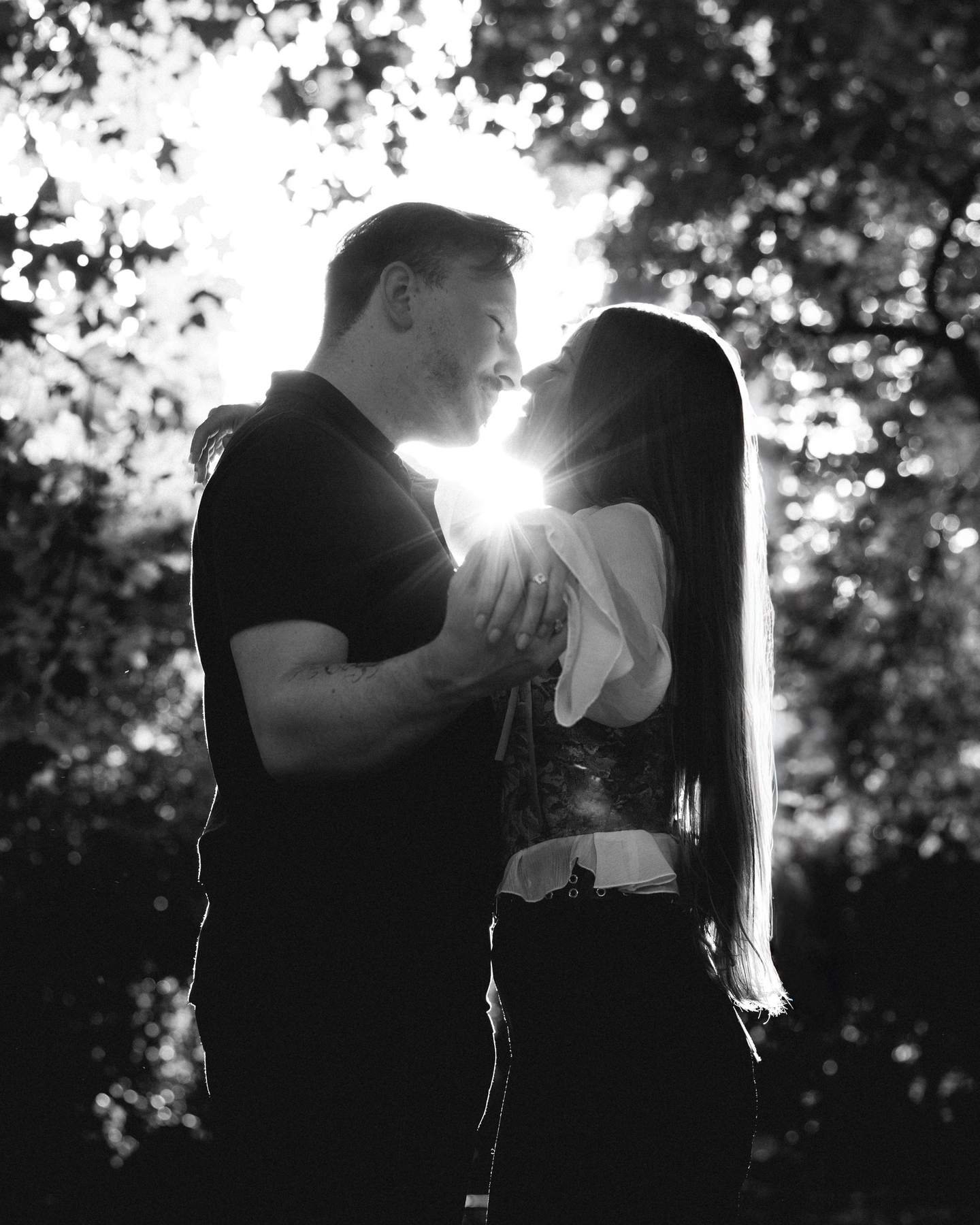 Black and white portrait of the couple kissing under the trees.