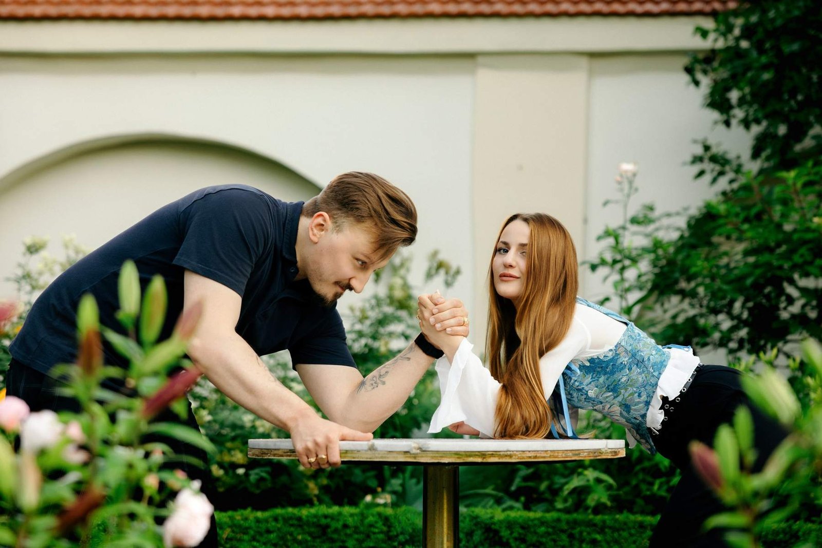 Couple laughing mid arm-wrestle at a small garden table.
