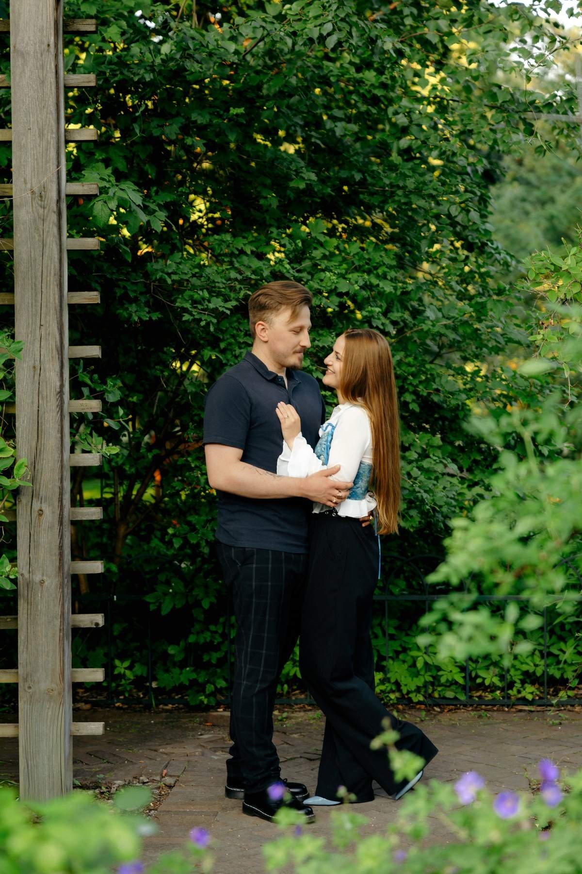 Couple standing together under a wooden pergola in Bernardinų Garden.