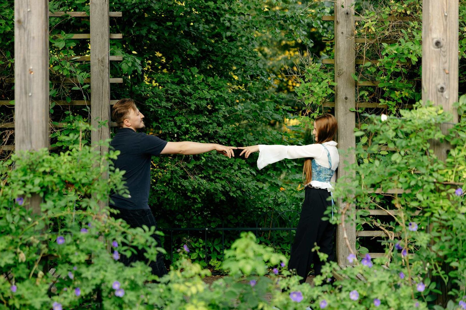 Newly engaged couple walking hand in hand through the garden pergola.