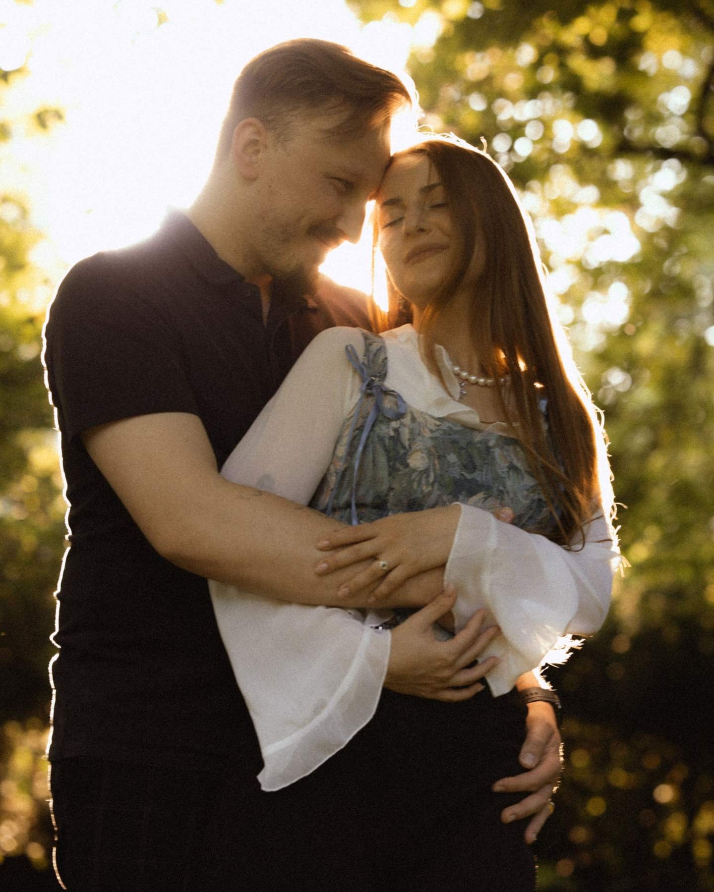 Newly engaged couple in a close embrace, eyes closed, golden hour light.