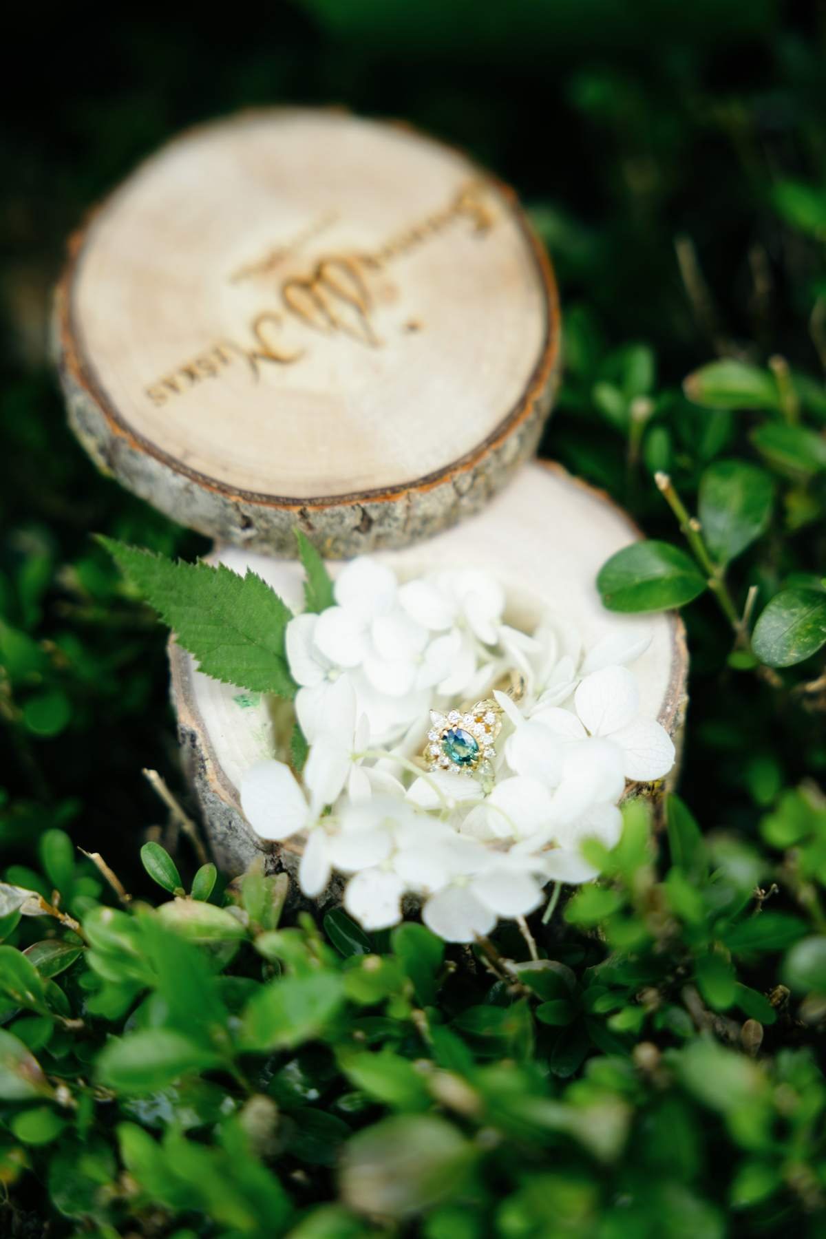 Engagement ring resting on a carved wood slice with a white flower.