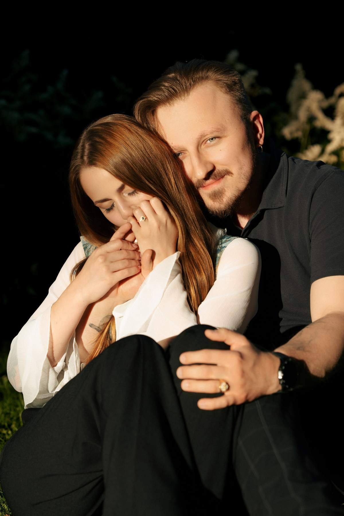 Evaldas hugging Brigita from behind while she laughs, sitting on the grass.