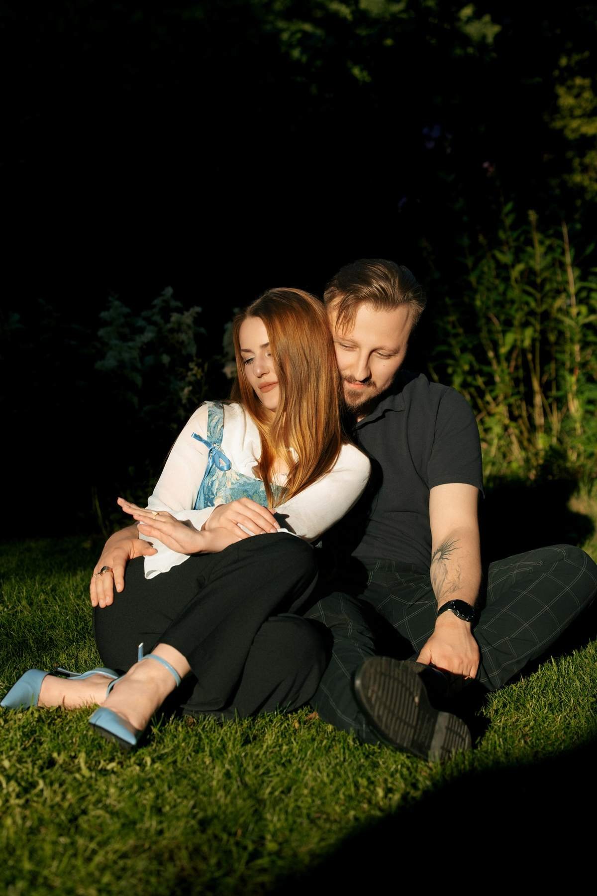 Newly engaged couple sitting close together on the grass in Bernardinų Garden.