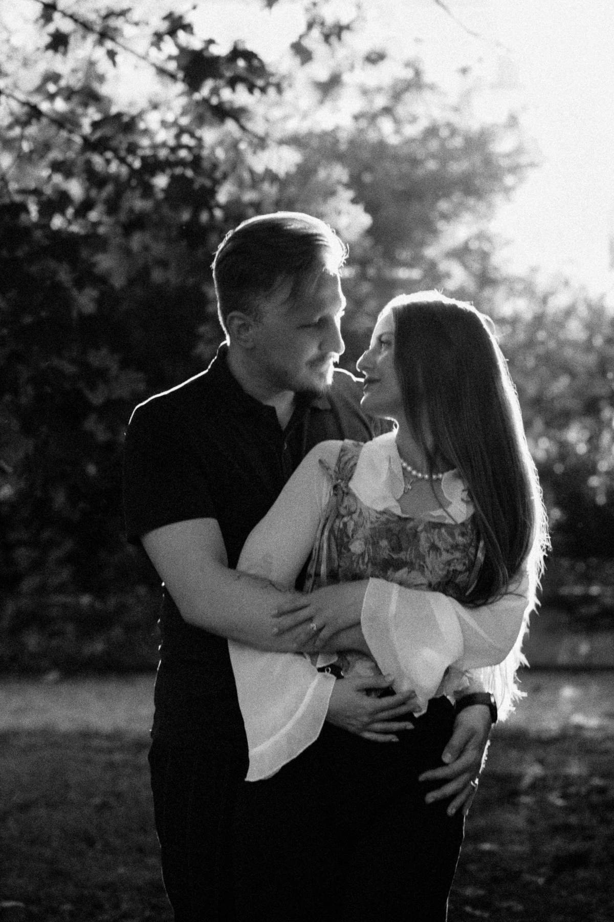 Black and white portrait of the couple embracing at sunset in the park.