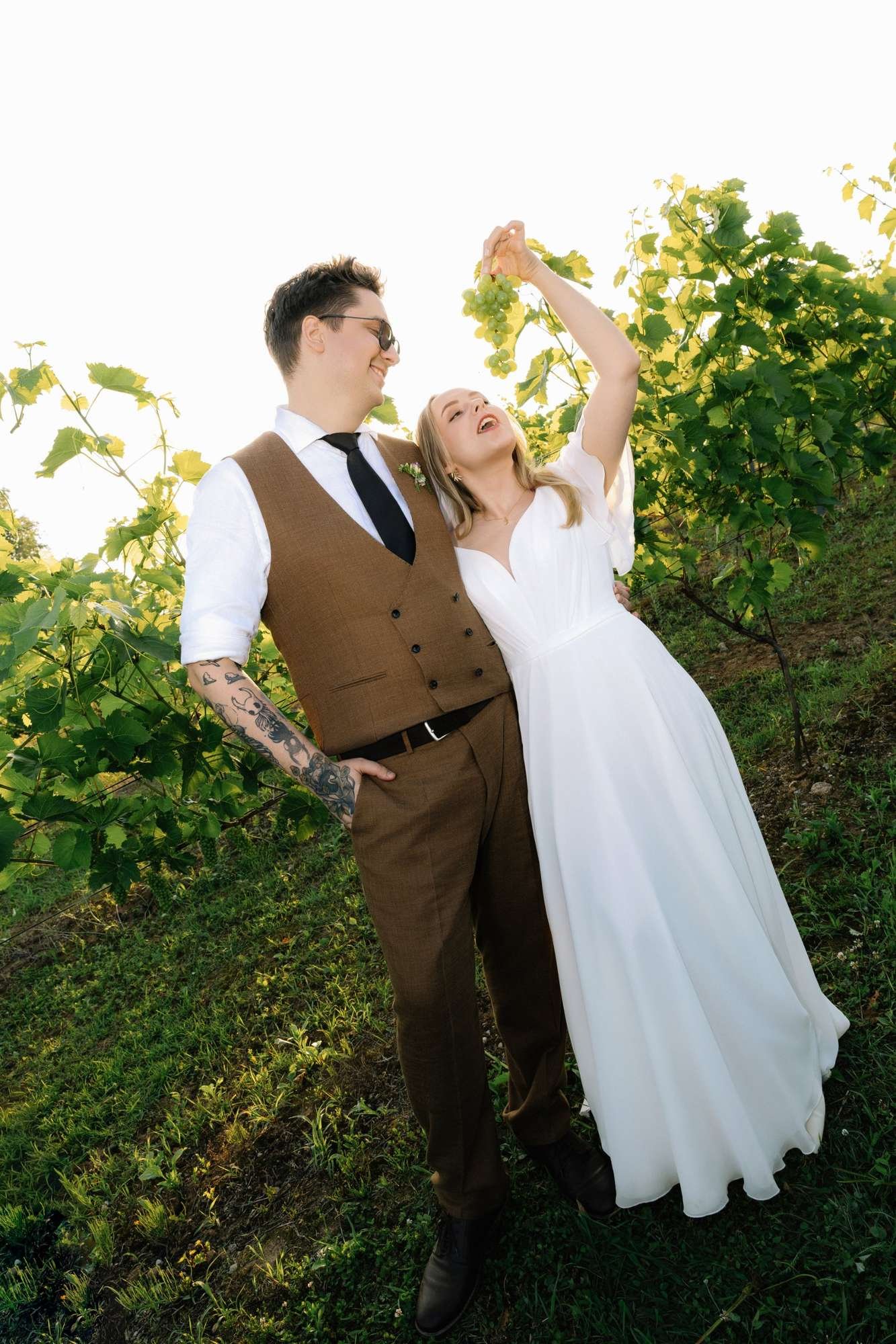 Bride laughing and trying to eat grapes while the groom smiles at a vineyard wedding in Italy (mobile cover photo)